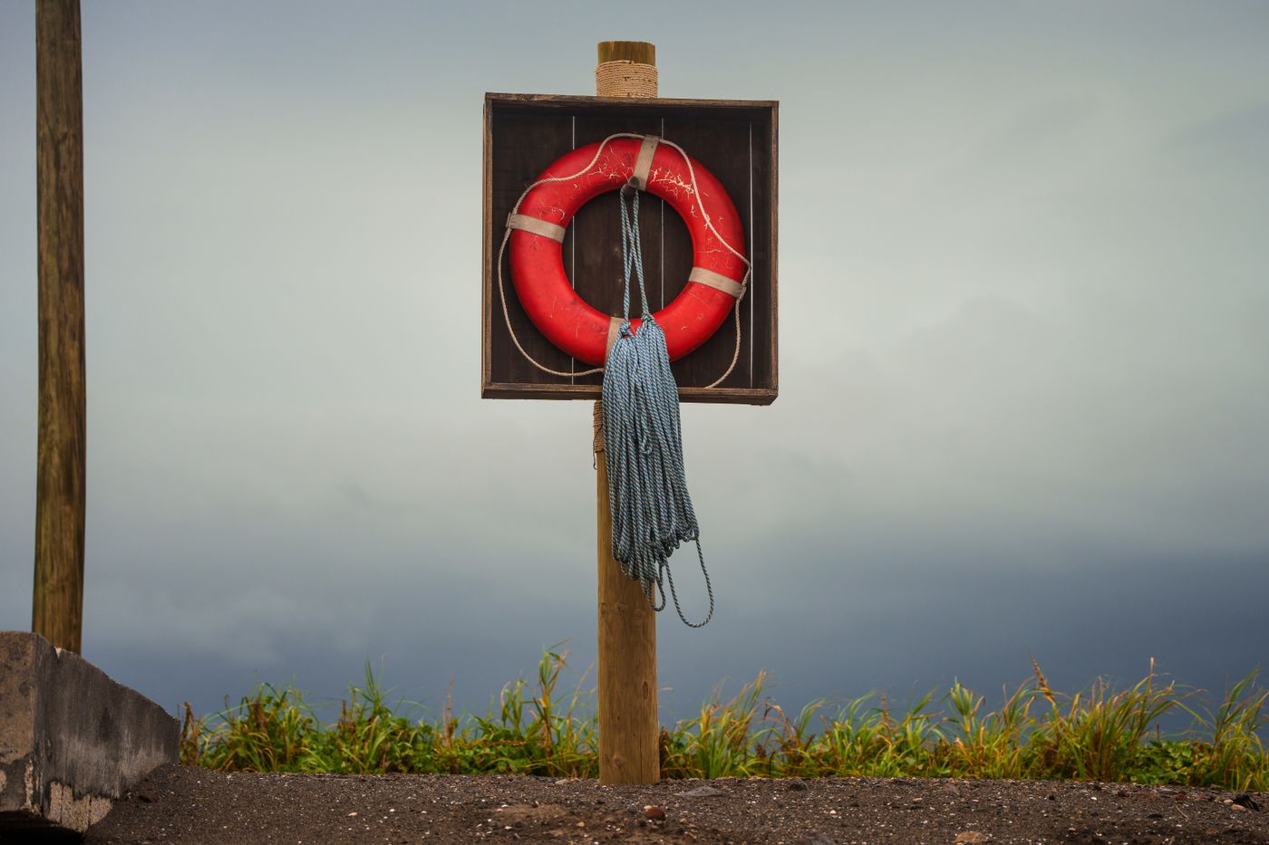 Boia salva-vidas vermelha presa a uma placa de madeira num poste, com o mar e um céu carregado de nuvens ao fundo, representando a reserva de emergência que fica guardada esperando o dia da tempestade