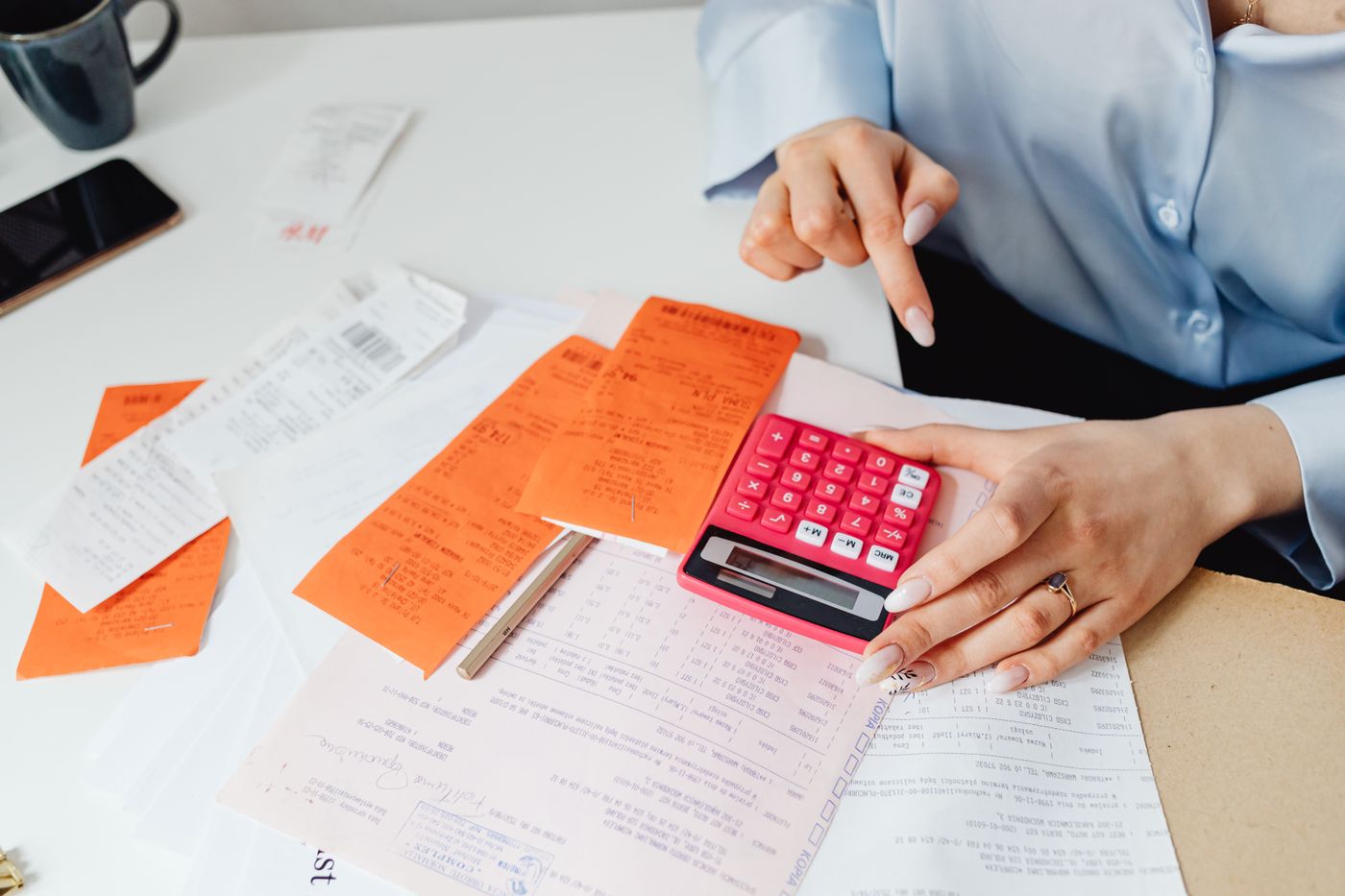 Mãos categorizando recibos coloridos e usando uma calculadora ao lado de um extrato bancário sobre a mesa