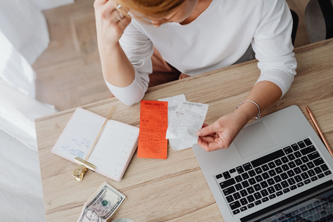 Mulher organizando recibos, notas e extrato financeiro sobre a mesa, ao lado do notebook, representando o levantamento de dados financeiros do cliente