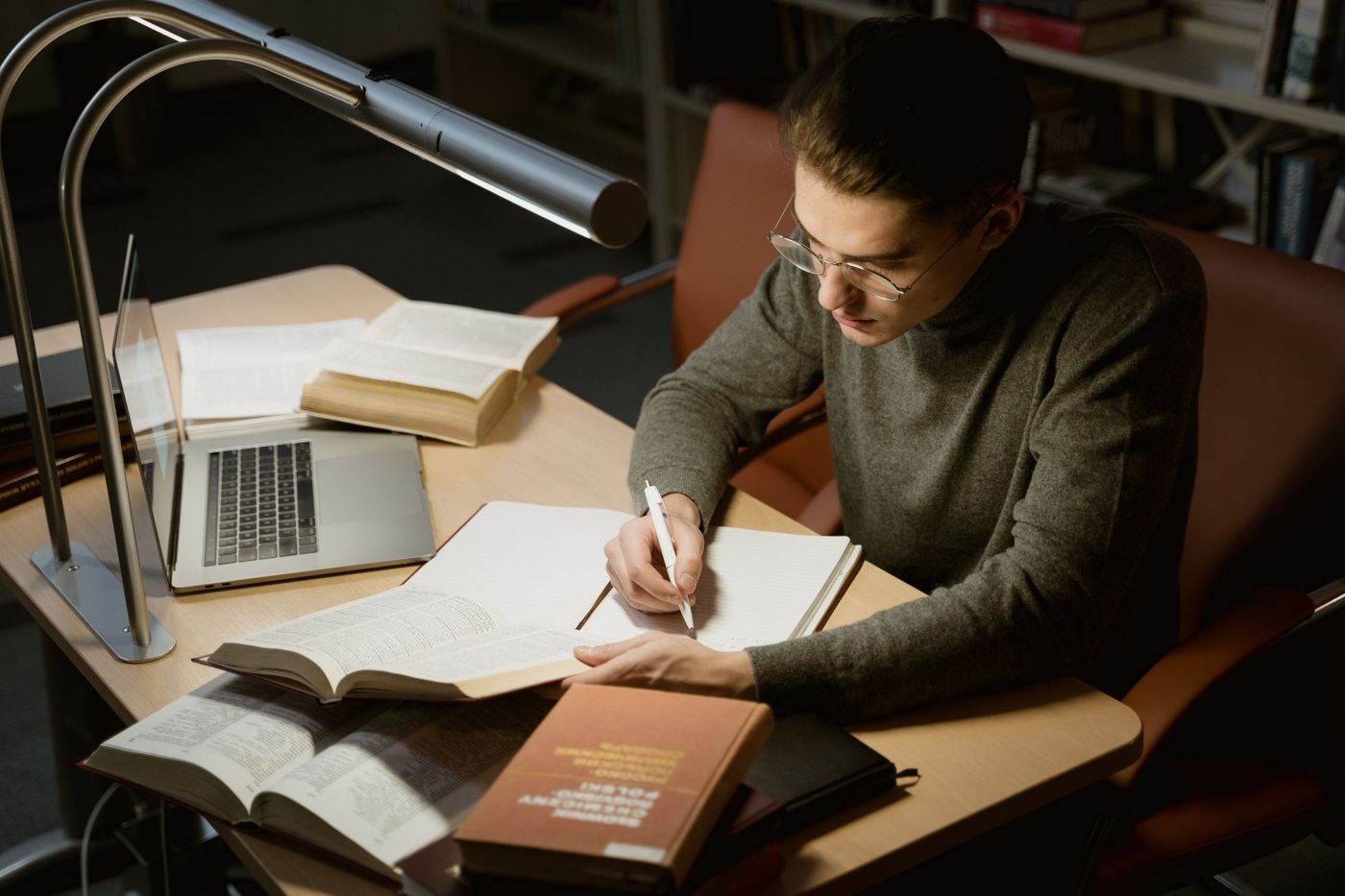 Homem estudando à noite com livros abertos, notebook e caderno de anotações sobre a mesa, representando o conteúdo que o futuro Educador Financeiro precisa dominar
