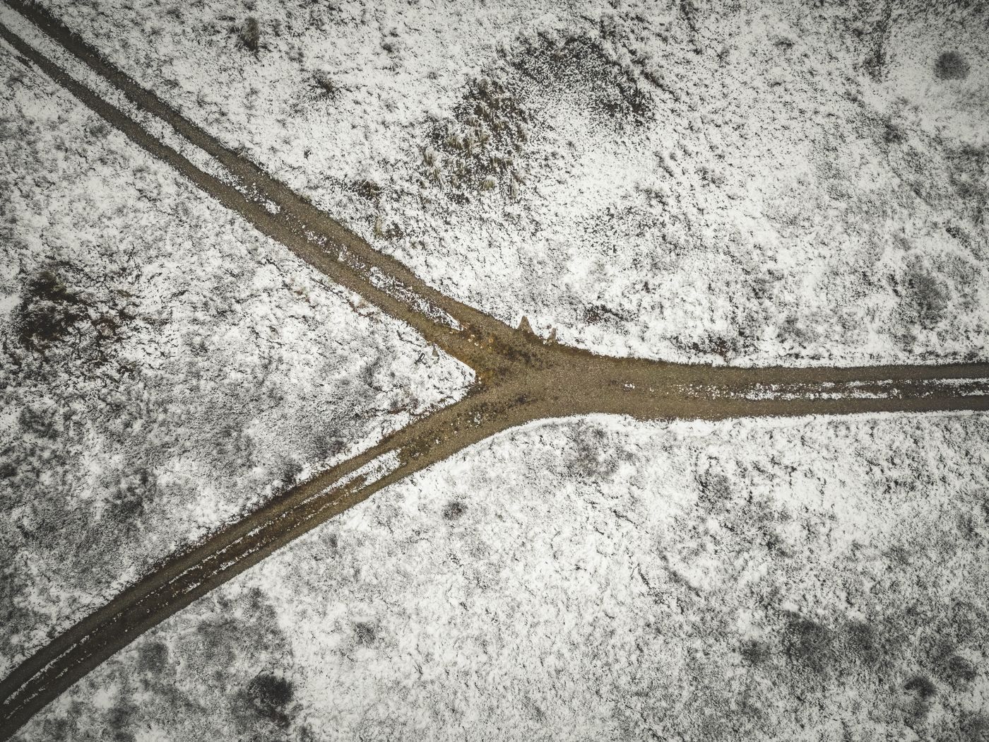 Vista aérea de uma estrada de terra que se divide em três caminhos sobre um campo coberto de neve fina, representando a escolha entre trilhas de formação