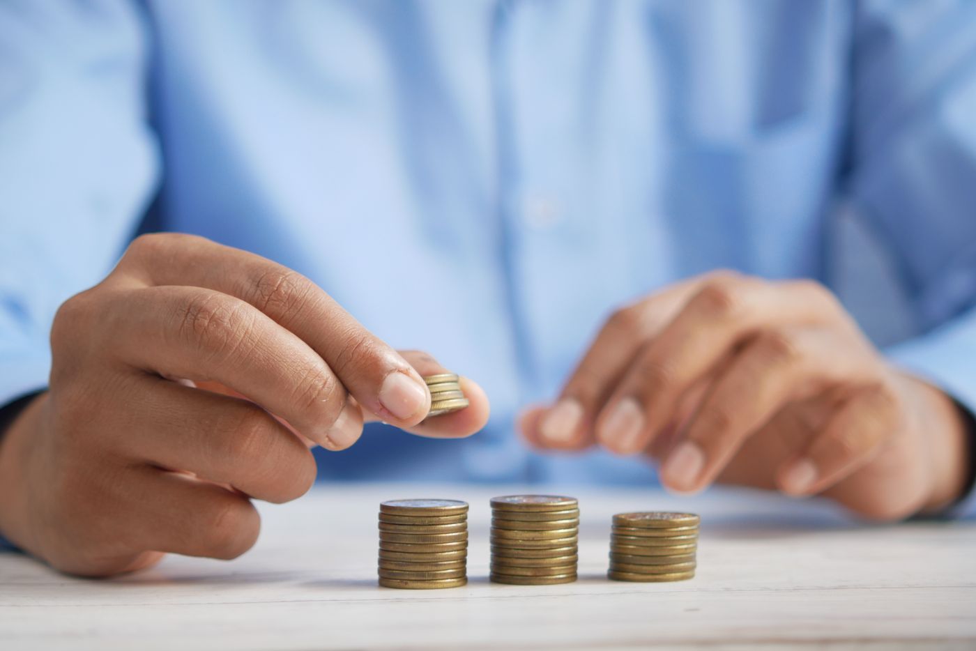 Mãos empilhando moedas em pilhas crescentes sobre uma mesa, representando o investimento financeiro necessário para tirar a certificação CFP