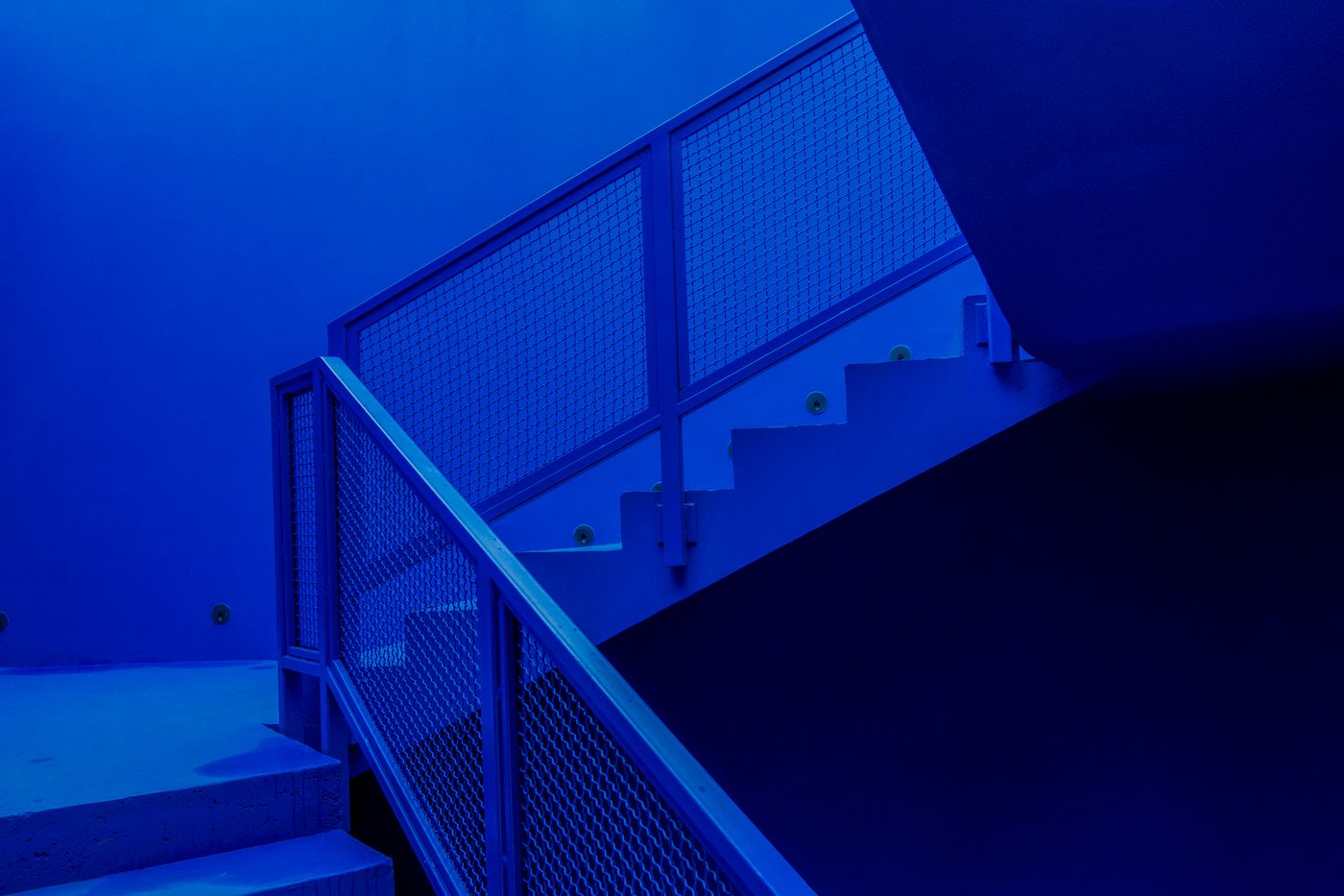 Escada de concreto com corrimão de metal subindo em um ambiente monocromático azul, representando os três degraus da esteira de serviços do Educador Financeiro